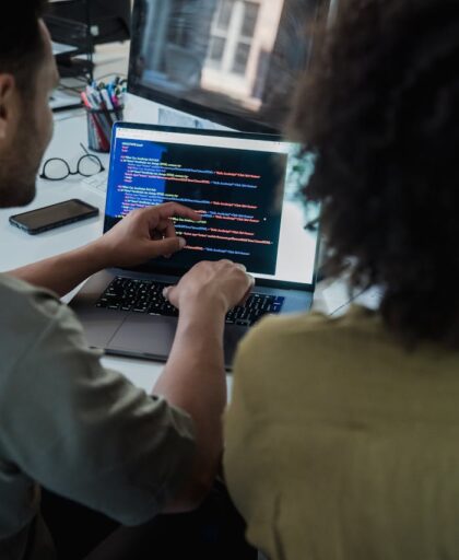 Two adults collaborating on programming tasks using a laptop in an office setting.