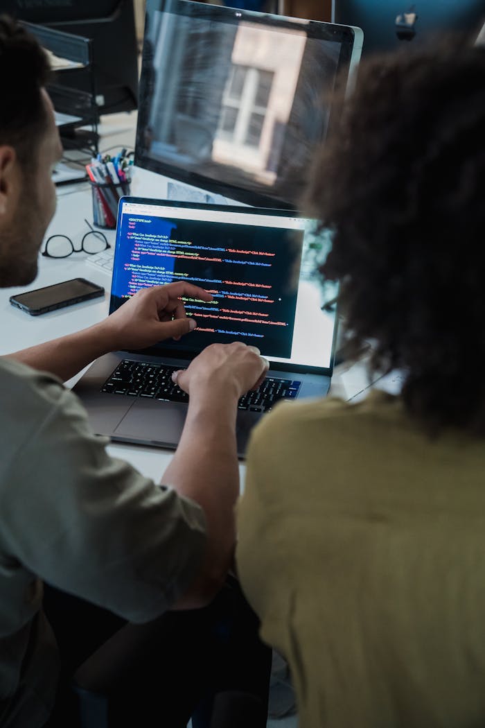 Two adults collaborating on programming tasks using a laptop in an office setting.